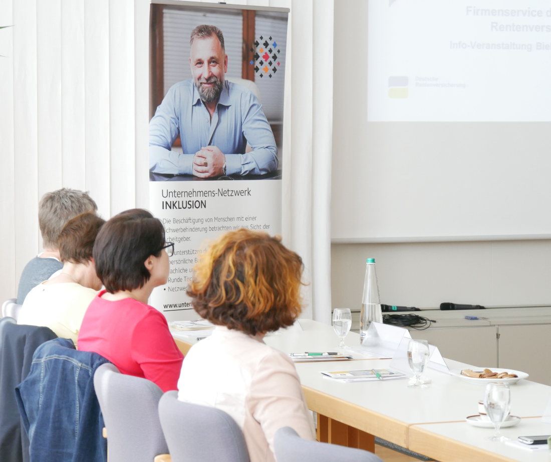 Menschen sitzen bei Veranstaltung und gucken nach vorn auf Präsentation.