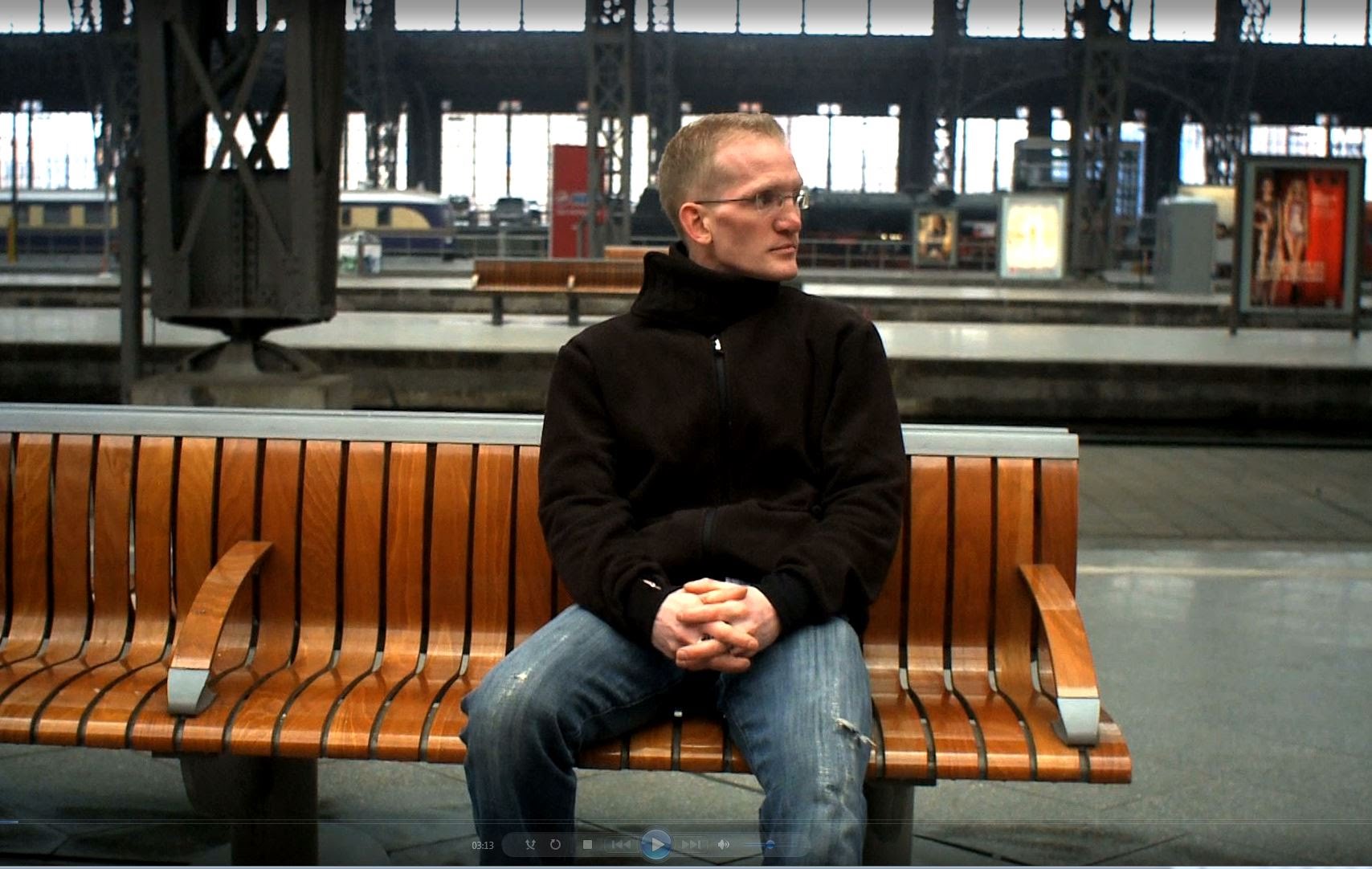 Mann sitzt auf Bank im Bahnhof.