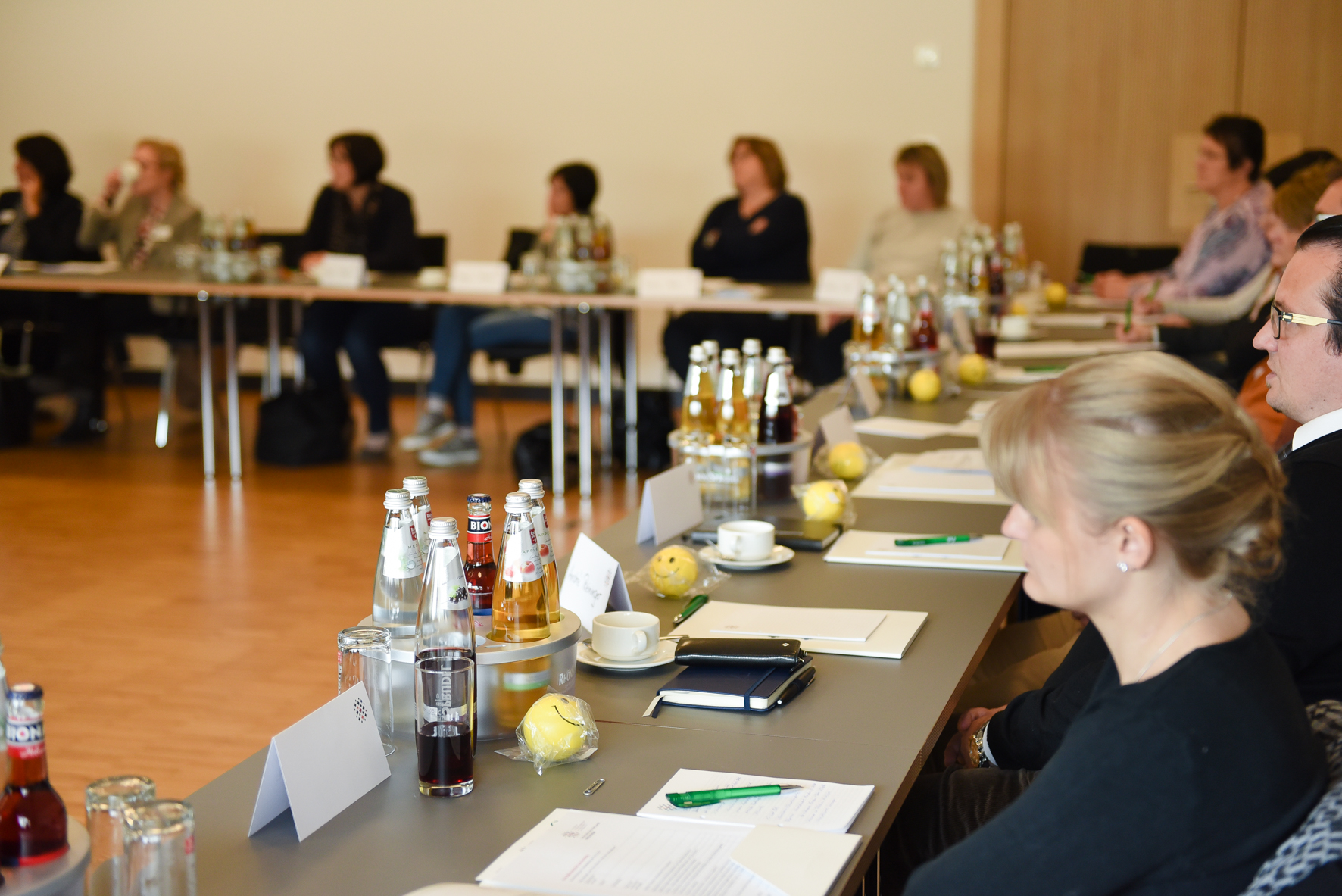 Menschen sitzen auf Stühlen an Tischen bei Veranstaltung.